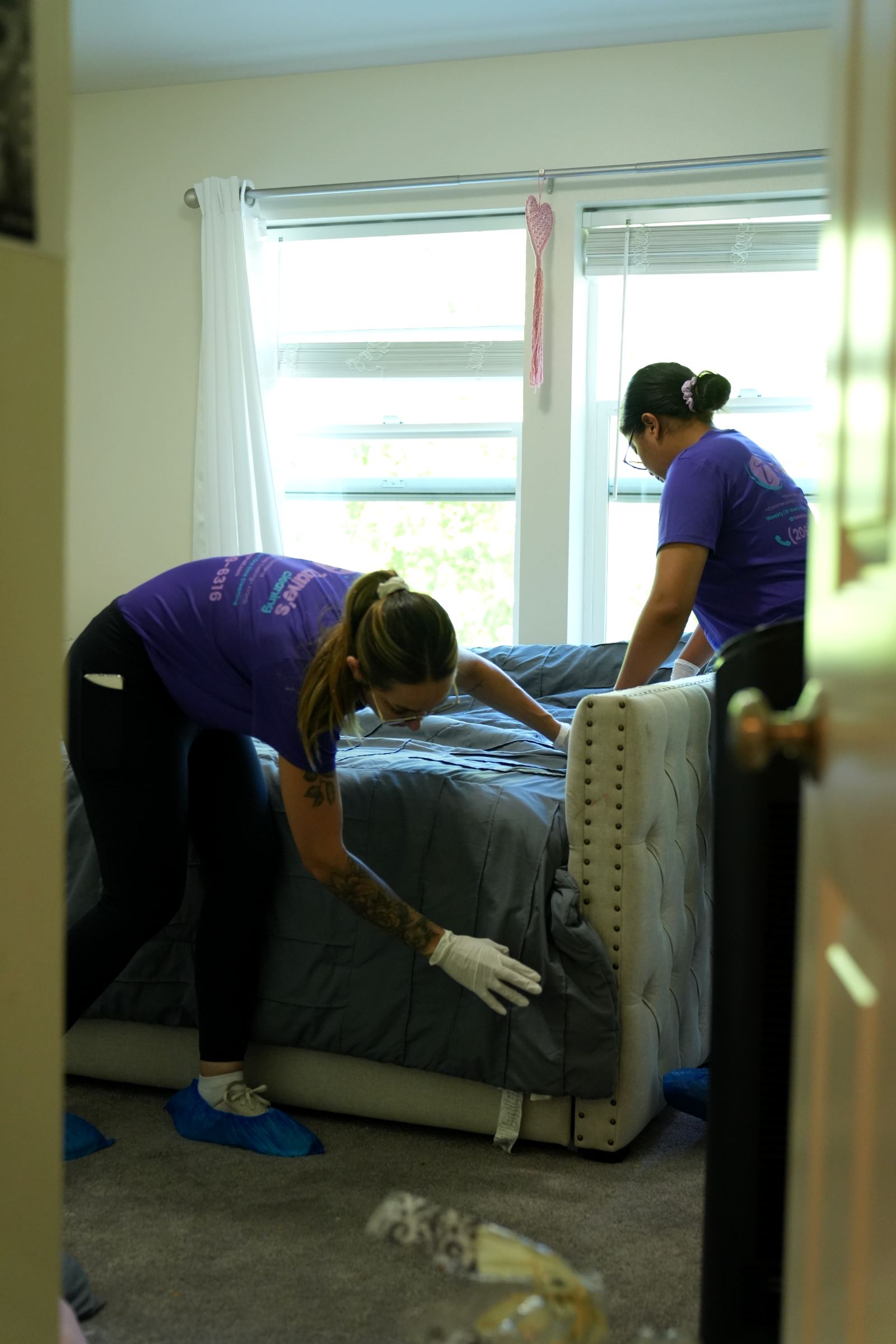 Two team members making a bed in a bright bedroom.